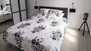 Quarto com cama, mesa de cabeceira, abajur, espelho e um tripé.