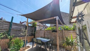 Um pátio com mesa e cadeiras, cerca de madeira e estrutura de pérgola.