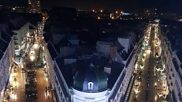 Um edifício histórico com uma cúpula central, rodeado por uma área pedonal com candeeiros e chão molhado.
