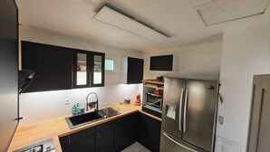 Uma cozinha compacta com armários pretos, uma geladeira de aço inoxidável, forno embutido e uma janela sobre a pia.