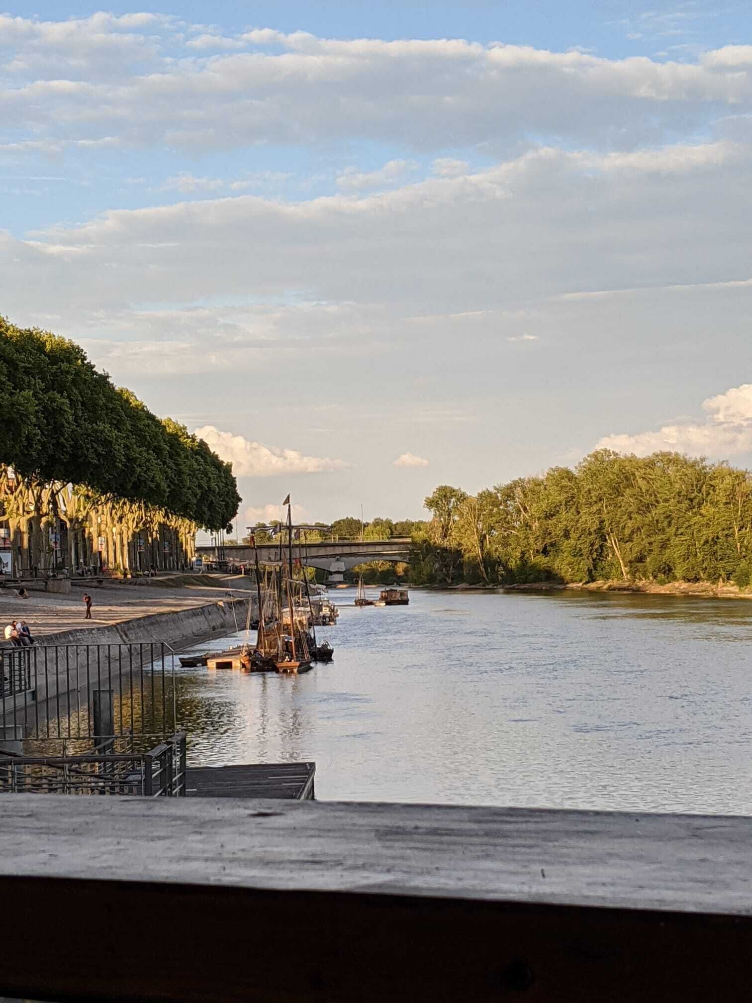 A riverside view with a bridge, docked boats, and a pedestrian walkway.