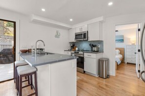 A modern kitchen with a central island, stainless steel appliances, and a view into the adjacent bedroom. - New Rental-3 beds, 2.5 baths, New Seabury (Mashpee)