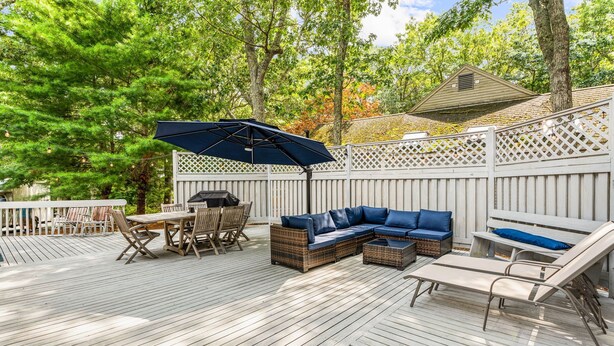 Eine Holzterrasse mit Gartenmöbeln, darunter ein Tisch, Stühle, eine Sitzecke und eine Bank.