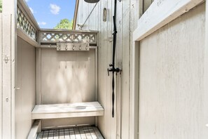 Ein kleiner, umzäunter Außenbereich mit einer Bank, einem Gartenschlauch und einem Metallrost auf dem Boden.