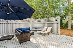 A deck with a wicker sofa and chairs, an umbrella, and a white fence. - New Rental-3 beds, 2.5 baths, New Seabury (Mashpee)