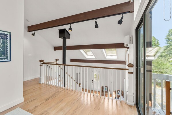Un intérieur spacieux avec un escalier en bois, des fenêtres de toit et une vue dégagée sur l’extérieur grâce à une porte vitrée.