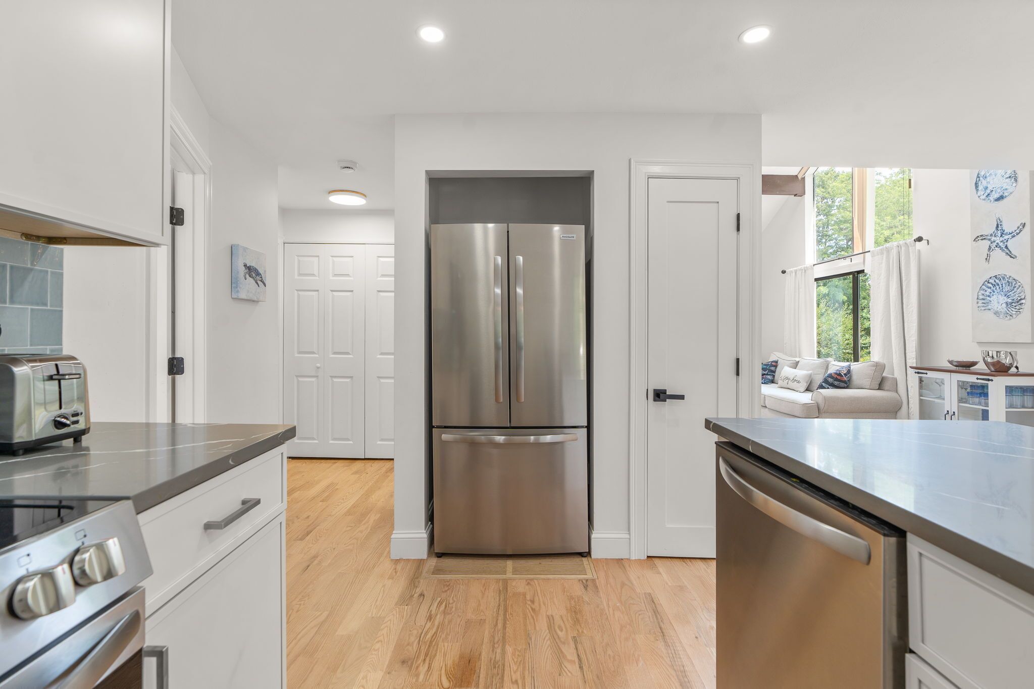 A modern kitchen with stainless steel appliances, a wooden floor, and a view of the outdoors through a window.