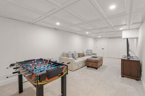 A room with a foosball table, a sofa, a coffee table, and a cabinet. - New Rental-3 beds, 2.5 baths, New Seabury (Mashpee)