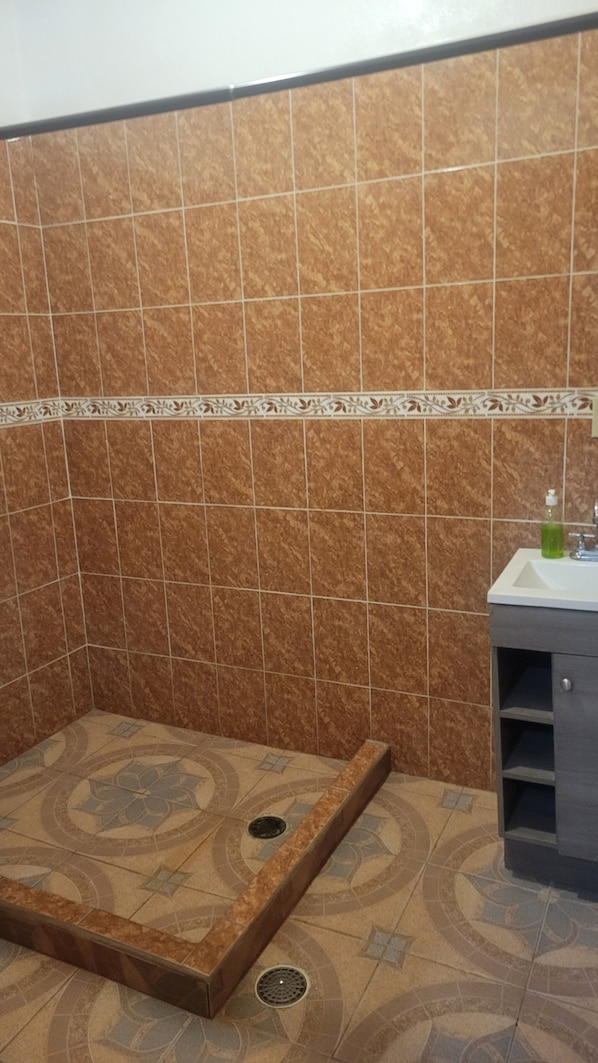 A bathroom with a shower area, a sink, and a cabinet.