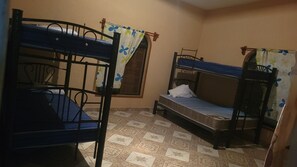Une chambre avec des lits superposés, une fenêtre avec des rideaux et des carreaux de sol à motifs.