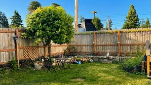 A fenced backyard with a tree, a wooden table, and a birdhouse. -  5-Min Walk to PSNS / 1,200 Sq Ft Furnished Suite / 30+ Nights / Pet Friendly (Bremerton)