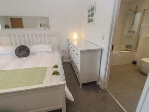 A bedroom with a bed, bedside table, dresser, and a bathroom with a shower. - Chy Holly (St Ives)