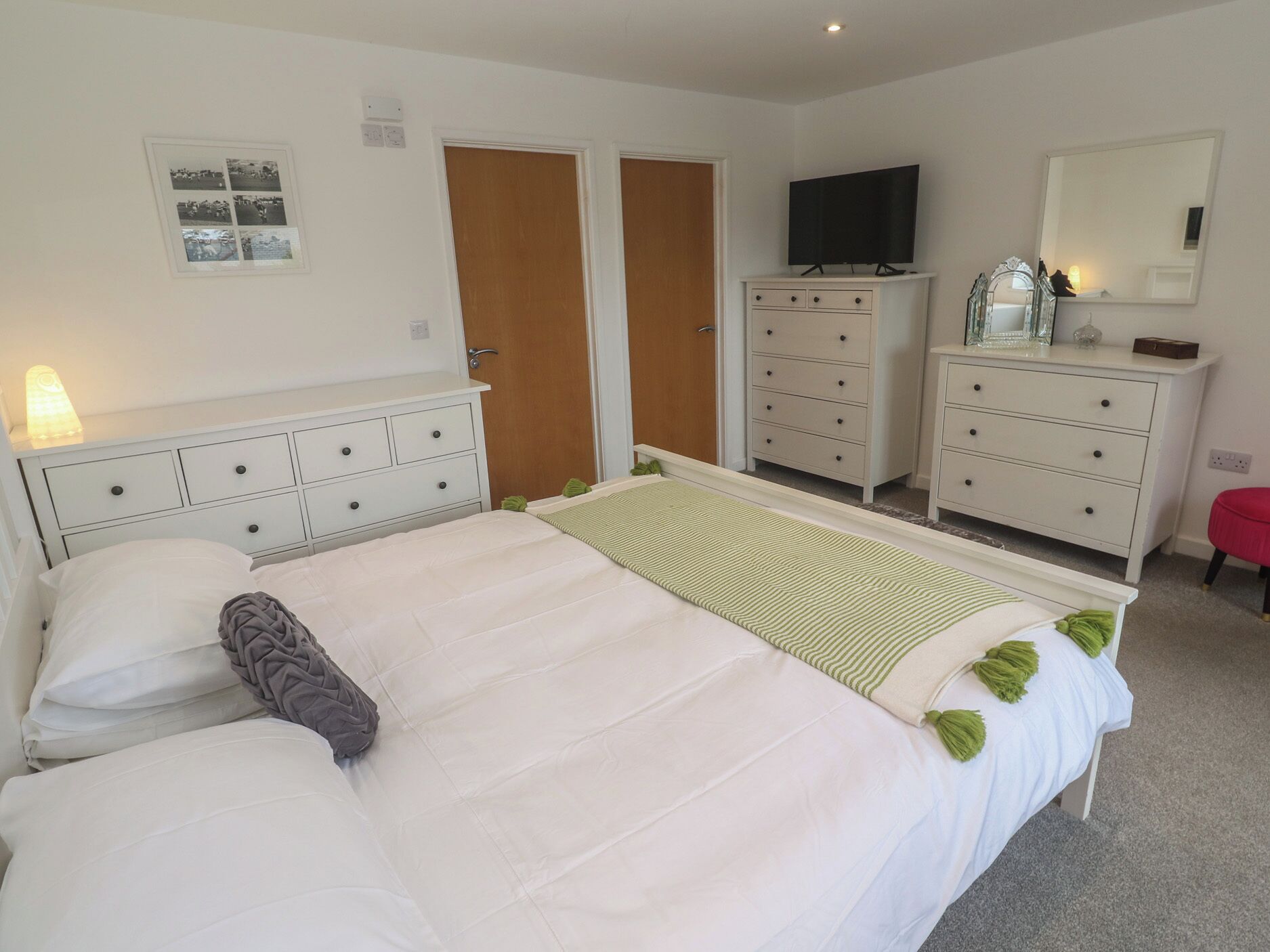 A bedroom with a bed, dresser, TV, and a mirror.
