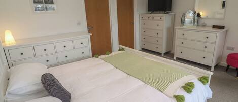 A bedroom with a bed, dresser, TV, and a mirror.