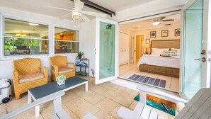 Una habitación con muebles de mimbre, una cama, un ventilador de techo y vistas a través de un ventanal.