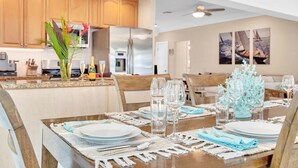 Un comedor con una mesa de madera dispuesta para una comida, una cocina con gabinetes de madera y un ventilador de techo.