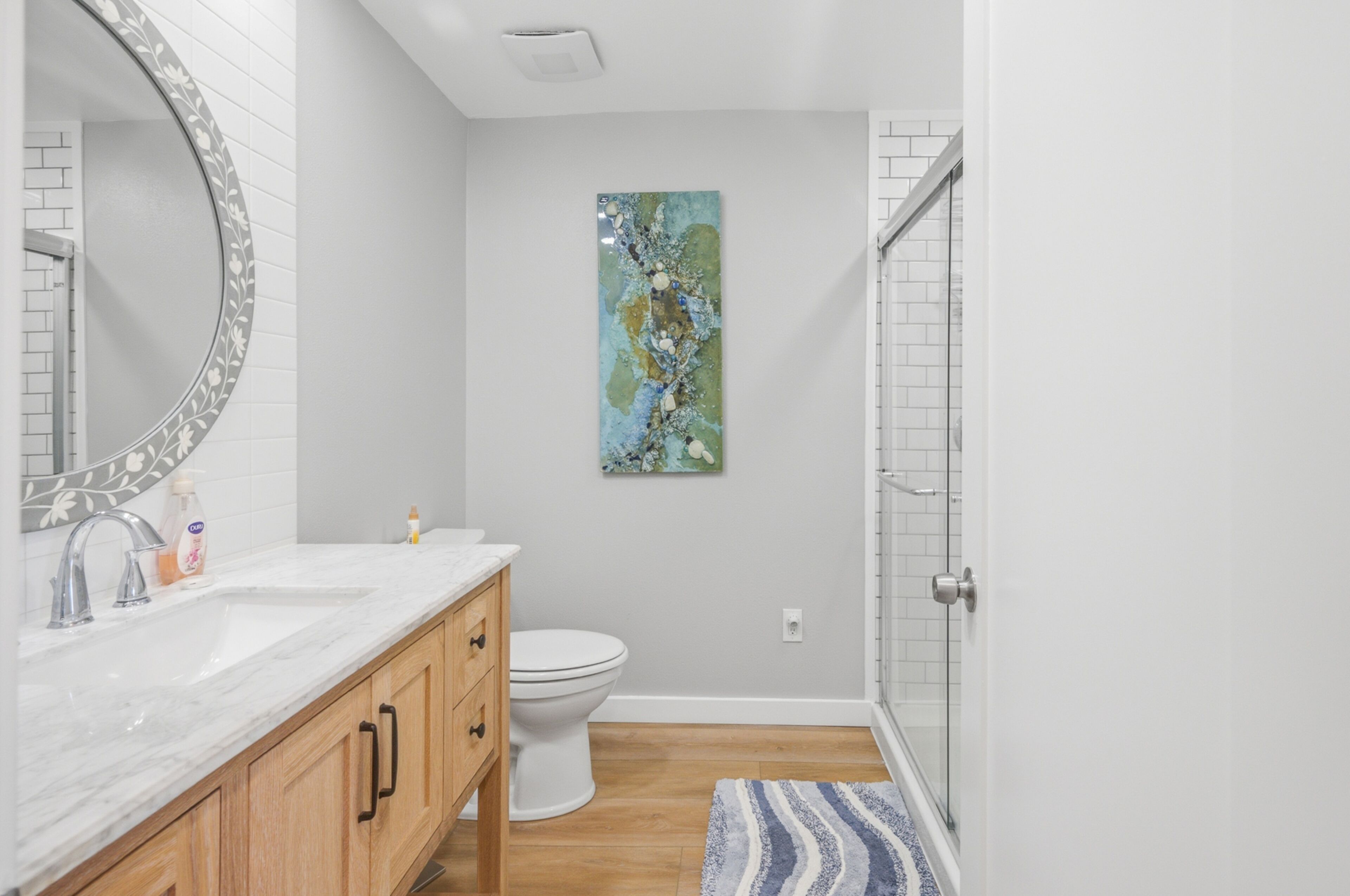 Une salle de bain avec des toilettes blanches, un lavabo avec un miroir, des meubles en bois et un espace douche.