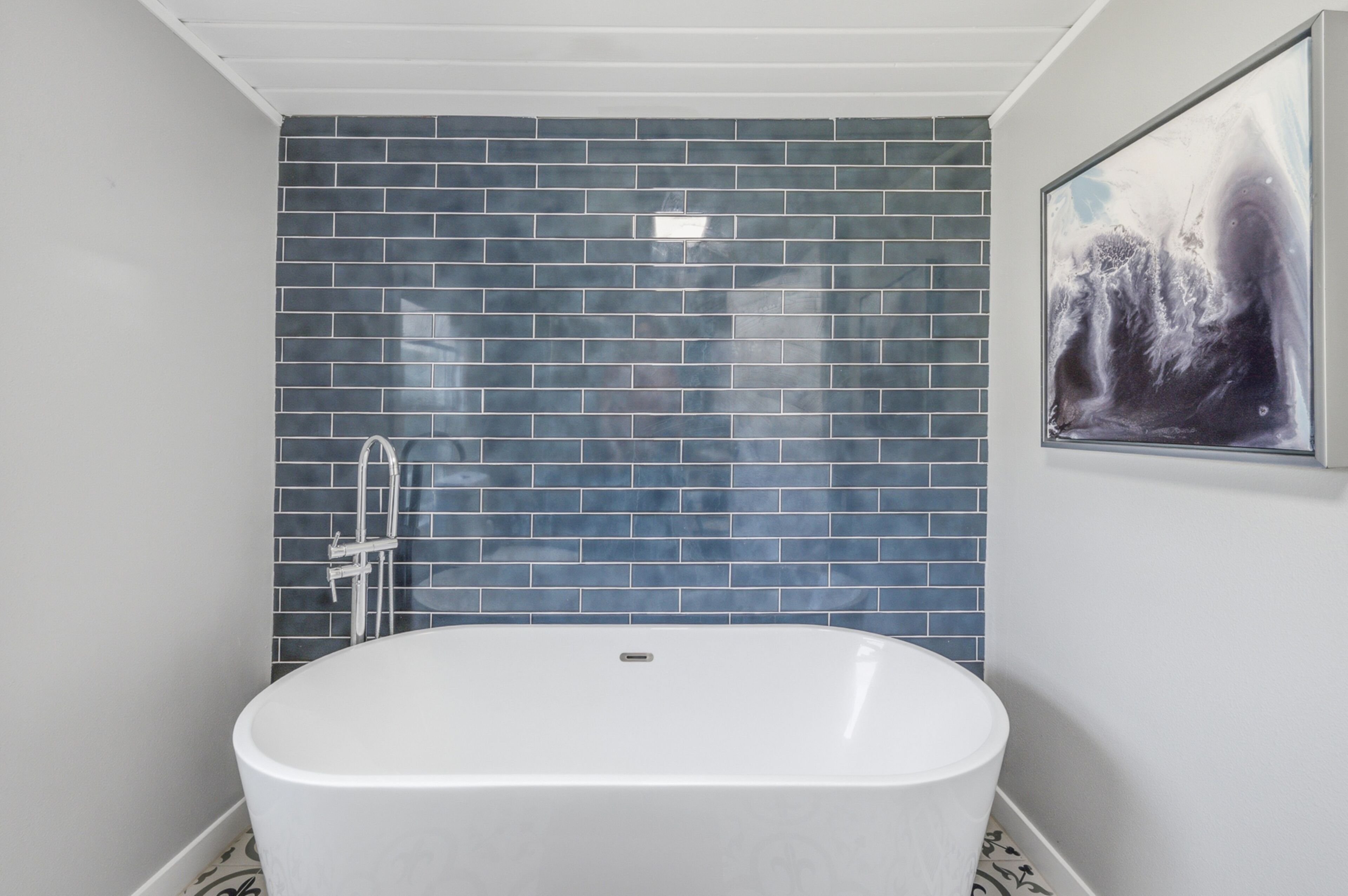 A bathroom with a white bathtub, a blue-tiled wall, and a framed picture.
