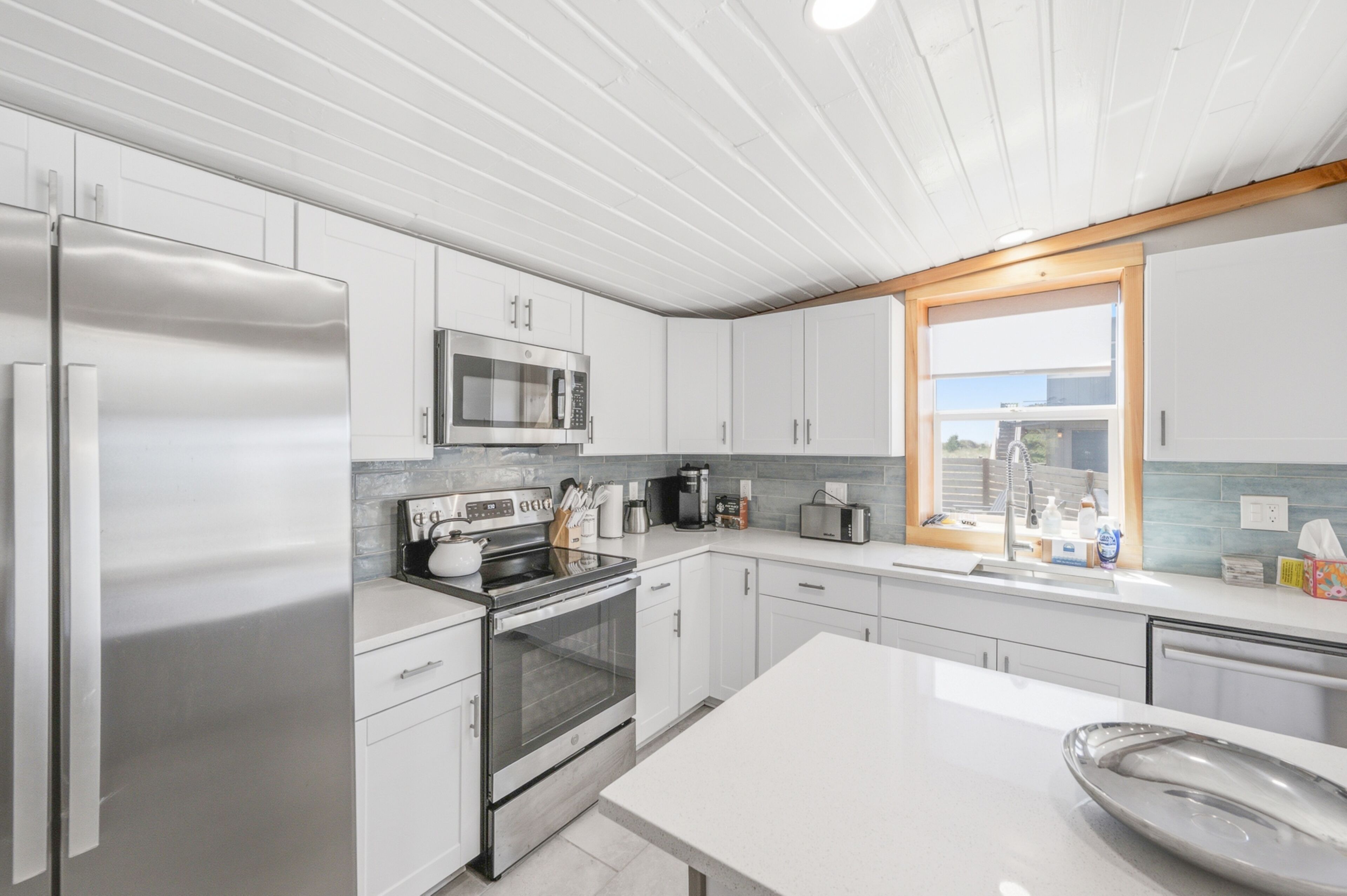 A modern kitchen with stainless steel appliances, white cabinetry, and a large window.