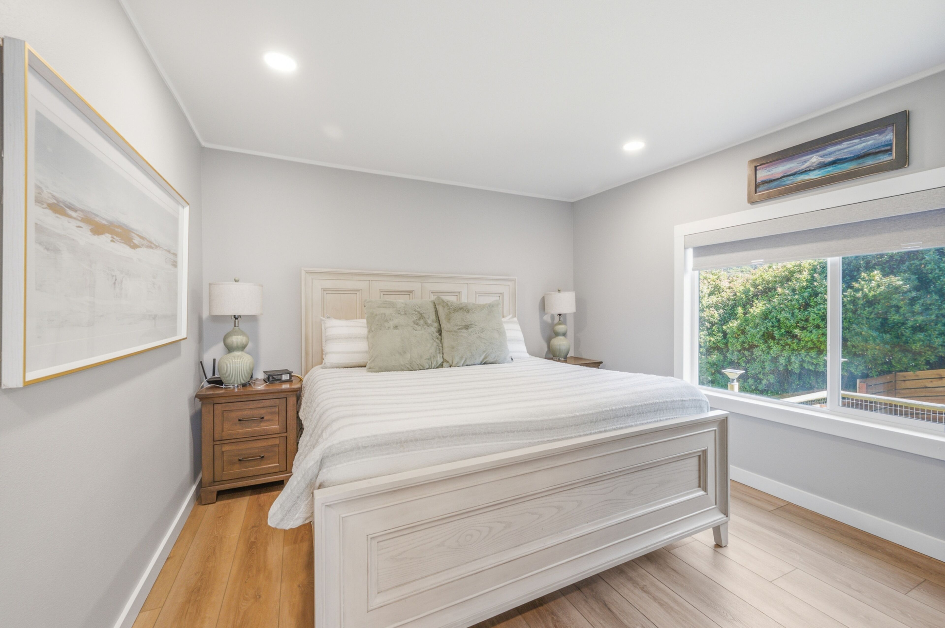 A bedroom with a bed, nightstands, a window with a view, and a framed picture on the wall.