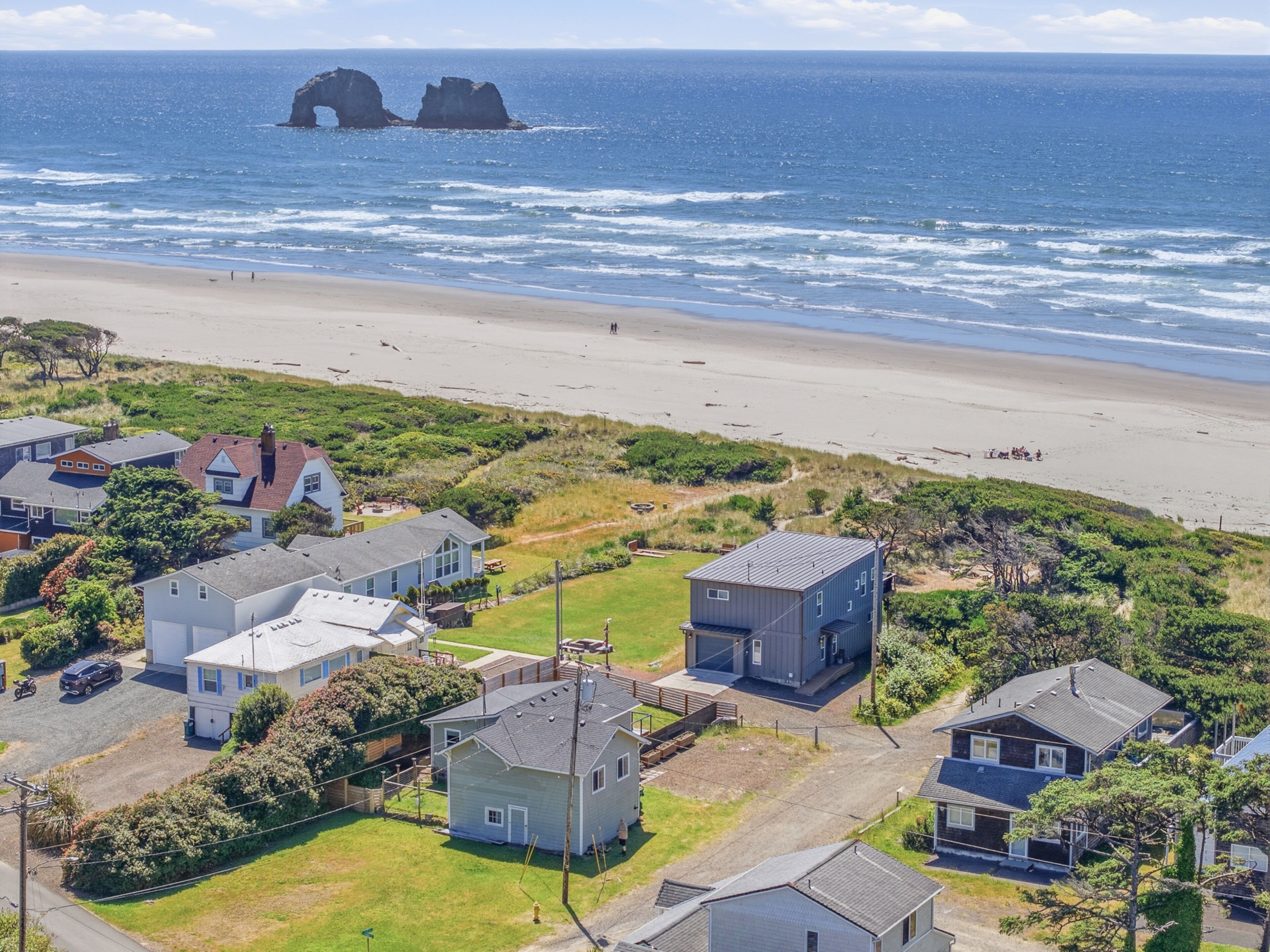Une zone résidentielle côtière, avec des maisons, une plage et une formation rocheuse particulière en arrière-plan.