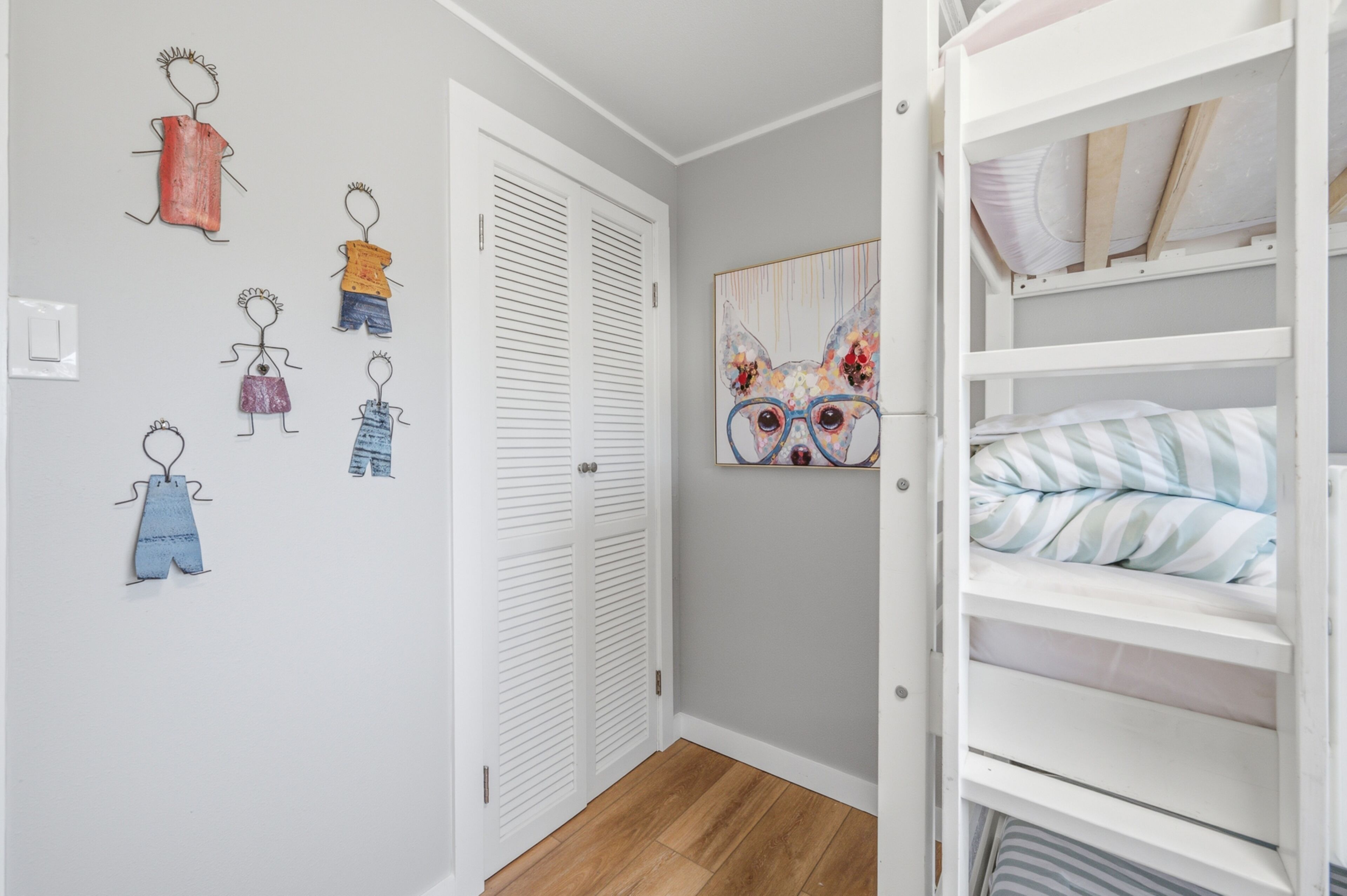 Habitación infantil con literas, una puerta con armario blanco y un muro con dibujos de niños.