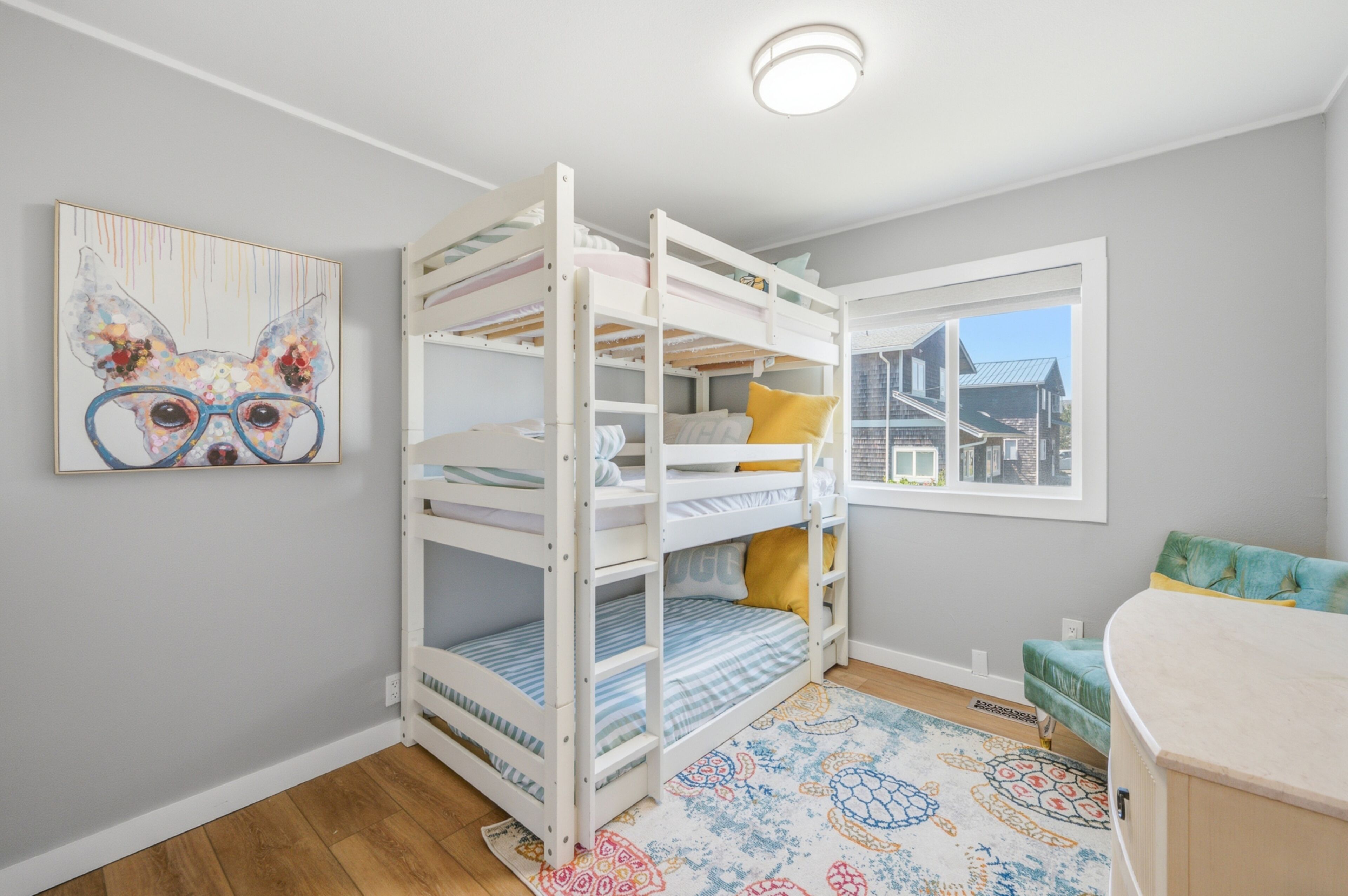 A bunk bed room with a window, a colorful rug, and a painting on the wall.