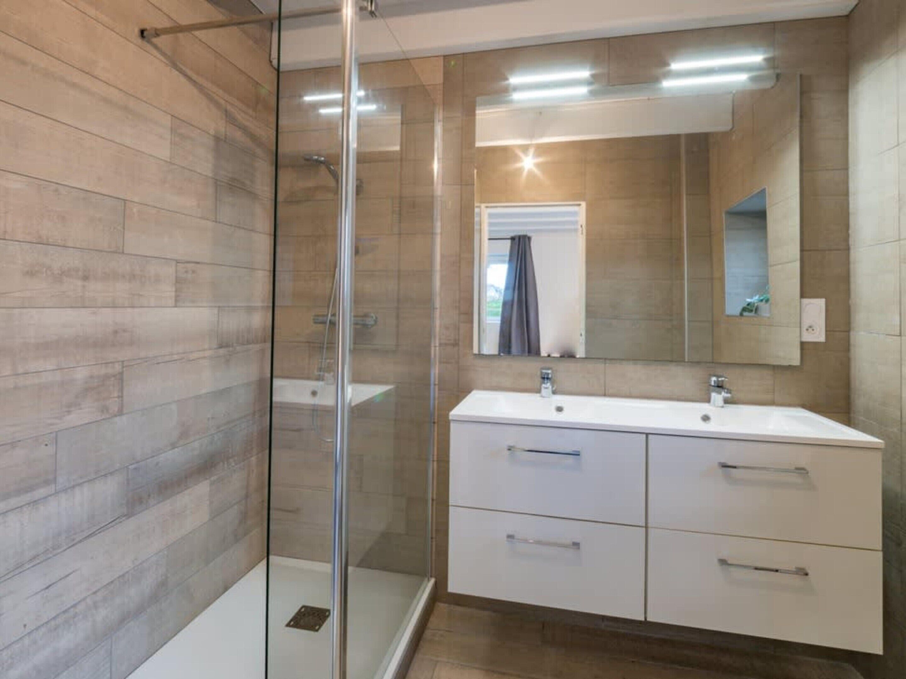 A modern bathroom with a glass shower enclosure, a white vanity with a mirror, and wooden flooring.