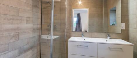 A modern bathroom with a glass shower enclosure, a white vanity with a mirror, and wooden flooring.