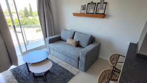 A living room with a grey sofa, a round table, and a dining area with chairs.