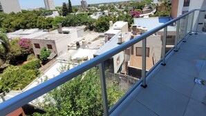 A balcony with a metal railing overlooking a cityscape with various buildings and greenery.