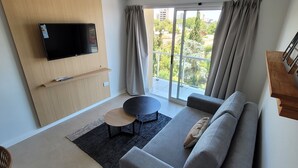 A modern living room with a flat-screen TV, grey sofa, and a small round table.