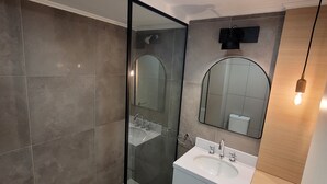 A modern bathroom with a glass shower enclosure, a white sink, and a wooden vanity.