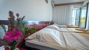 A hotel room with a large bed, a bedside table, a vase with flowers, and a window with curtains. - Hotel Issa - Triple Room Sea View (Vis)