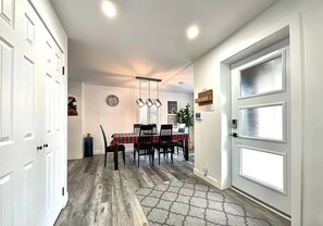 A hallway with a dining area, white doors, a clock, and a 'BONJOUR' sign. - The 1568 in Charlevoix (Petite-Rivière-Saint-François)