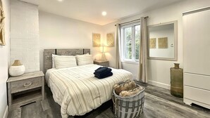 Ein Schlafzimmer mit Bett, Nachttischen, Lampe, Spiegel, Fenster und Korb.