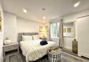 A bedroom with a bed, nightstands, a lamp, a mirror, a window, and a basket. - The 1568 in Charlevoix (Petite-Rivière-Saint-François)