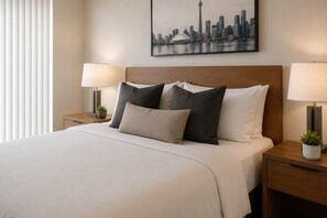 Ein Hotelzimmer mit einem Bett, zwei Nachttischen mit Lampen, einem Stadtbild an der Wand und einem Fenster mit Jalousien.