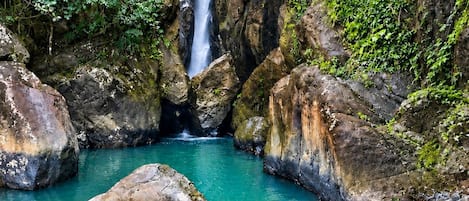 A natural landscape with a waterfall, clear water, and a person swimming.