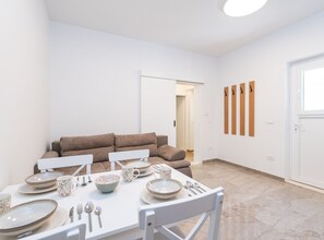 Ein Essbereich mit einem weißen Tisch, gedeckt für vier Personen, einem braunen Sofa und einer weißen Wand mit Holzpaneelen.