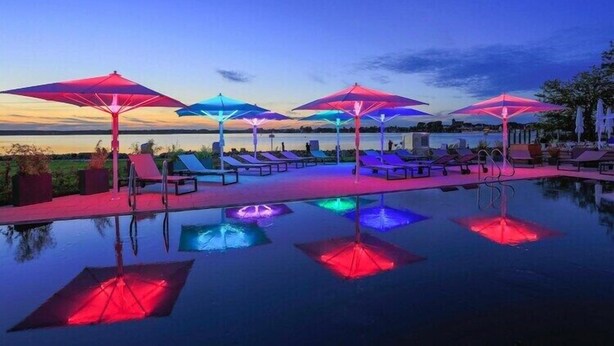 Une piscine à débordement avec des parasols colorés et des chaises longues, le tout baigné par les couleurs du coucher de soleil.