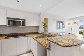 A modern kitchen with white cabinetry, granite countertops, a built-in microwave, and a large island with a sink. - Waterfront serenity in the heart of the city… (San Juan)
