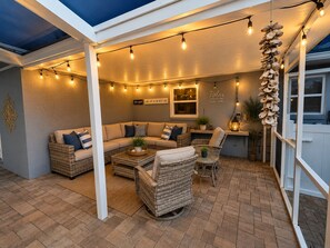 Ein Sitzbereich im Freien mit einer Couch, Sesseln und einem Tisch, unter einer überdachten Terrasse mit Lichterketten.