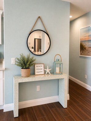 A hallway with a light blue wall, a round mirror, a framed picture, a console table with a potted plant, a starfish decoration, and a sign that reads 'BEACH HOUSE HAPPY'. - Crystal River waterfront oasis w/floating dock 3BR/3BA house, large heated pool (Crystal River)