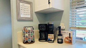 Uma bancada de cozinha com cafeteira, máquina Keurig, porta-cápsulas de café e caixa Keurig Café.
