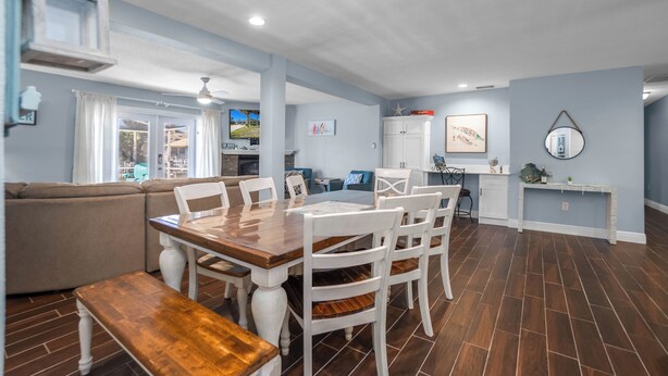 Uma sala de estar ampla com uma mesa de jantar, cadeiras brancas, um sofá e uma cozinha.