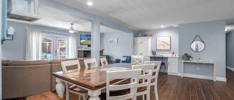 A spacious living area with a dining table, white chairs, a sofa, and a kitchen area.
