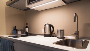 Una cucina moderna con lavello in acciaio inossidabile, bollitore, una bottiglia di vino e macchina per il caffè.