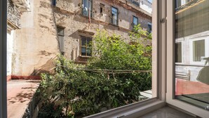 Vista attraverso una finestra di un edificio con numerose finestre, alcune dotate di persiane, e un balcone con ringhiera in metallo.