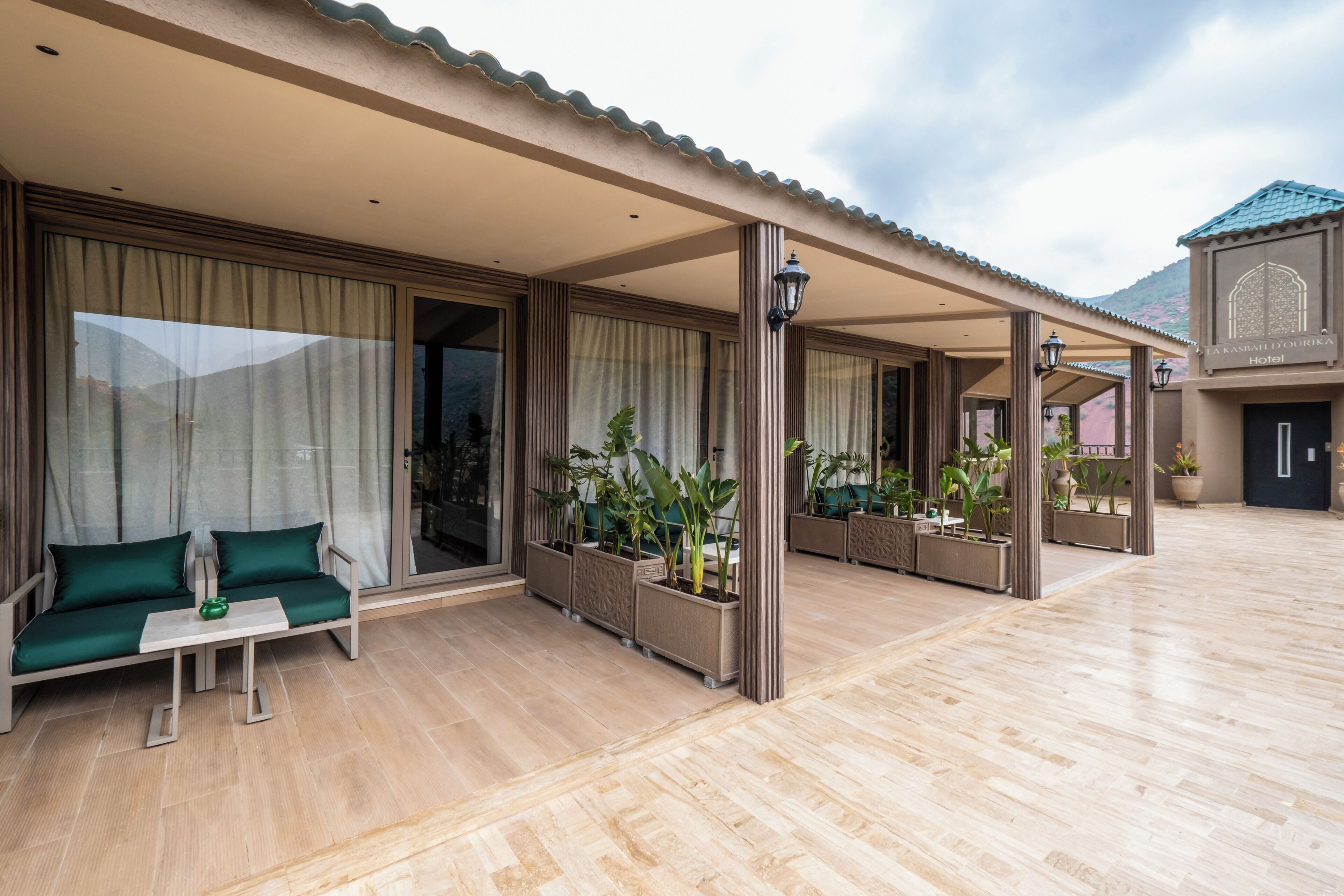 Un hotel con una zona de estar al aire libre cubierta, ventanas amplias y plantas en macetas.